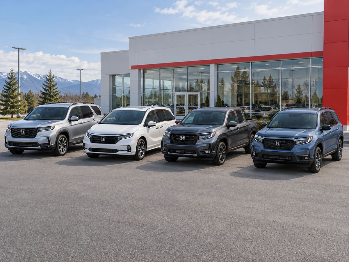 Four Honda vehicles lined up in a paved lot in front of a glass-fronted building: a silver SUV, a white minivan, a dark grey pickup and a blue SUV