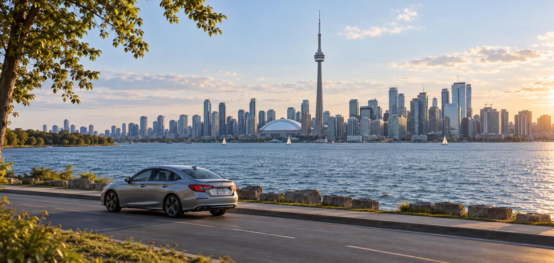 View of the Toronto skyline and its tall tower across a lake, with a silver Honda sedan on the waterfront road