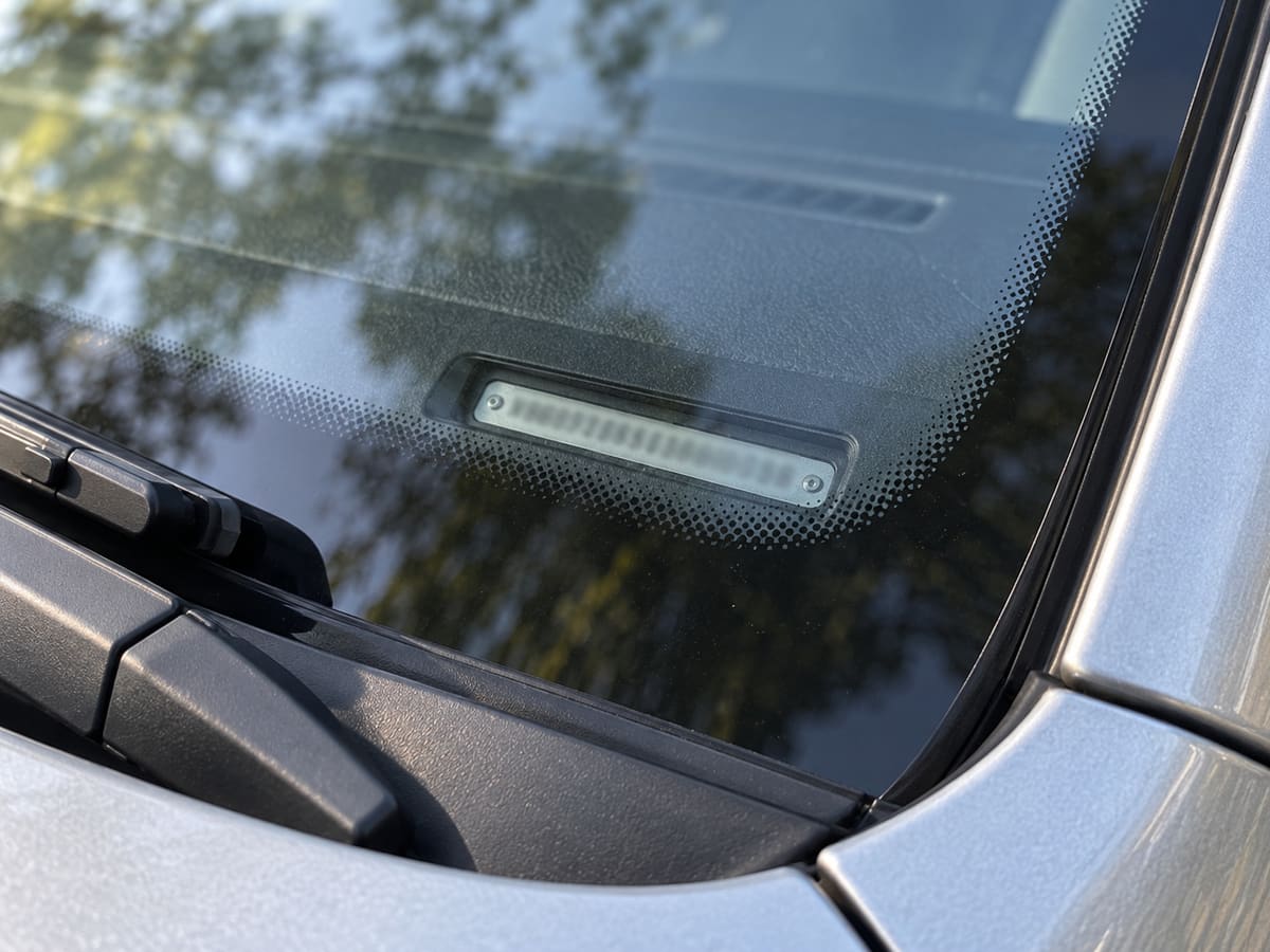 View through the windshield at the driver’s side showing the small VIN plate at the base of the glass, with its characters blurred